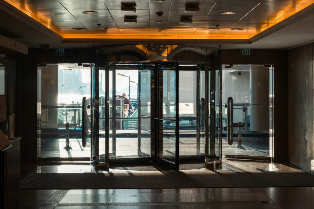 Interior shopping mall lobby with revolving glass doors; Balenciaga storefront on the right and warm orange ceiling lighting above.