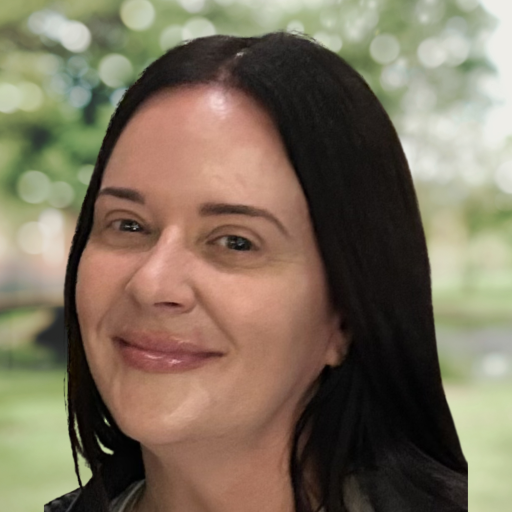 Close-up of a woman's face with a gentle smile, outdoors with a leafy green blurred background.