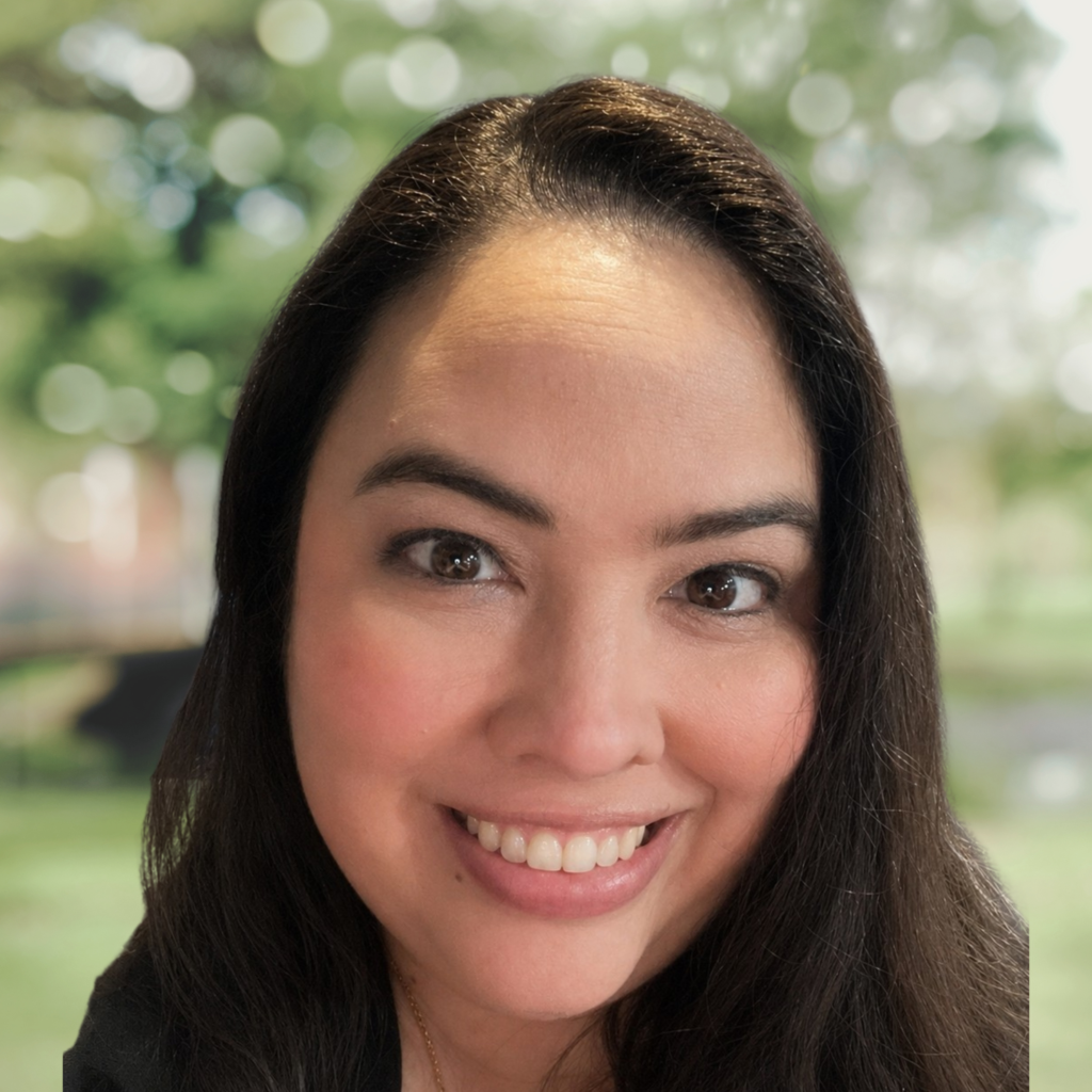 Close-up of a smiling woman's lower face outdoors with green, blurred background.
